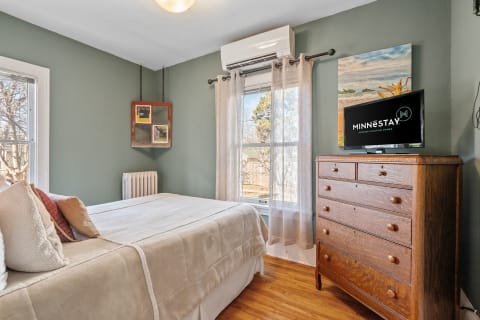 A cozy bedroom with green walls, wooden furniture, and a bed adorned with colorful pillows.