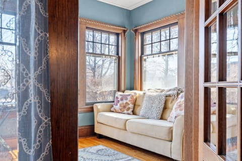 A cozy living room with a beige sofa and decorative pillows next to large windows.
