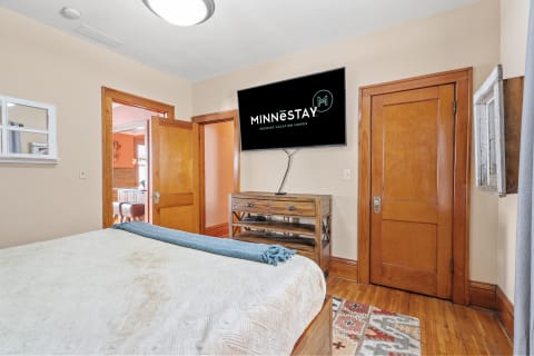 A bedroom with a bed, wooden accents, and a TV displaying MINNESTAY logo.