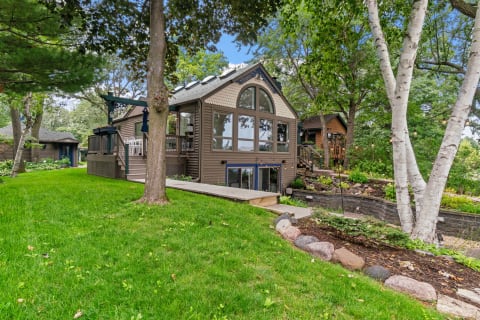 A lakeside cottage surrounded by trees and a well-manicured lawn.