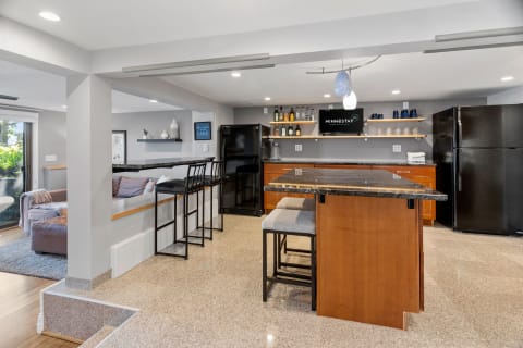 Modern kitchen with a granite island, bar stools, a black refrigerator, and a cozy sofa.