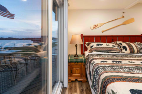Cozy bedroom with a red headboard, bear-themed bedding, and a view of a lake through a sliding glass door.