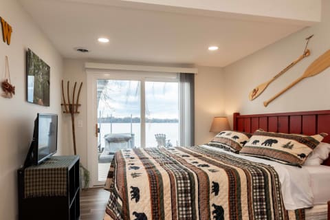 A bedroom featuring a bear-patterned quilt, a flat-screen TV, and sliding glass doors overlooking a lake.
