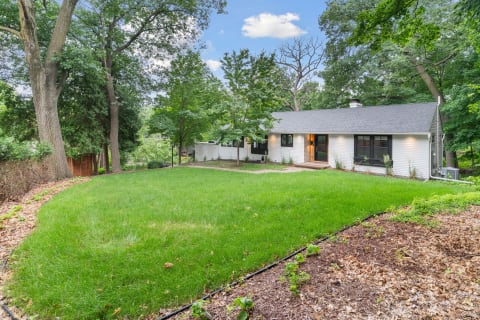 A contemporary house with a white facade and green lawn, set among trees.