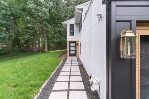 Pathway made of concrete slabs and gravel leading to a modern home surrounded by trees.
