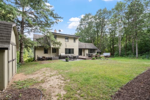 A two-story house with a deck, grill, and a spacious backyard surrounded by trees.