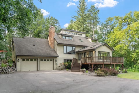 A stylish home with a two-car garage, wooden deck, and surrounded by trees on a sunny day.
