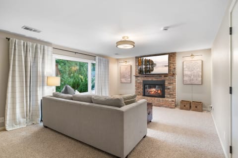 Cozy living room with gray sofa, brick fireplace, and large window.