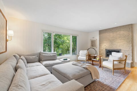 A cozy living room with a gray sectional sofa and large windows overlooking greenery.