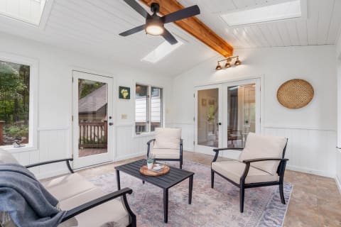 A light-filled sunroom with two armchairs, a coffee table, and a view of greenery outside.