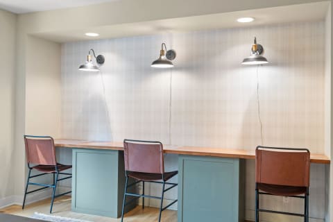 A modern workspace featuring a wooden countertop and industrial style lights above three leather chairs.