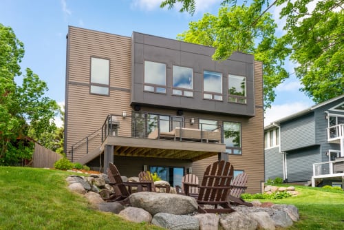 Modern vacation home featuring contemporary architecture with natural wood and stone elements in a tree-lined neighborhood setting.