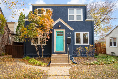 Charming blue house with bright turquoise door surrounded by beautiful autumn foliage in a quiet residential neighborhood.
