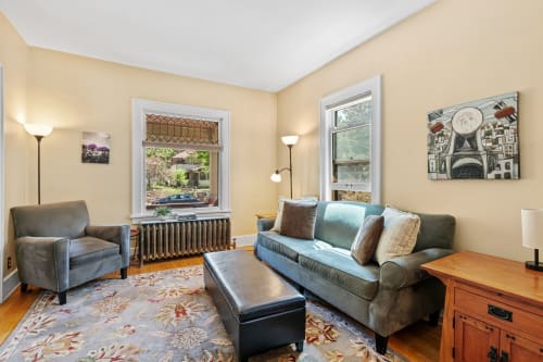 Relax in your cozy living space with comfortable seating, warm lighting, and charming street views through large windows.