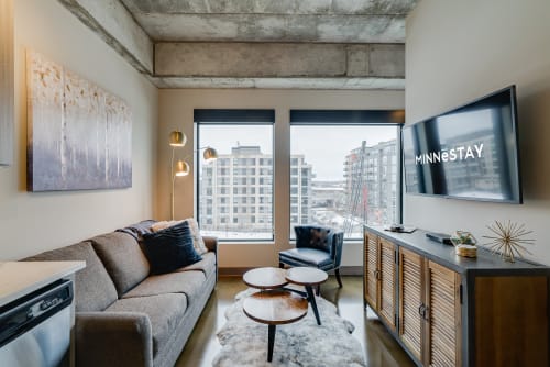 Unwind in your modern living space with exposed concrete beams, plush seating, and stunning city views through floor-to-ceiling windows.