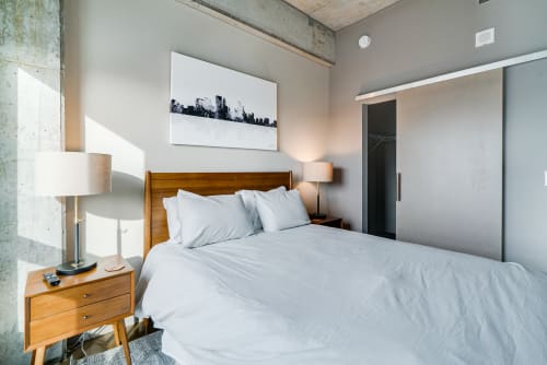 Sink into crisp white linens in your modern bedroom, where warm wood tones and industrial chic create perfect urban tranquility.